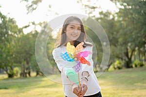 Young Beautiful Asian Woman holding the colorful windmill toward the camera with big happy smile feeling carefree and happy with