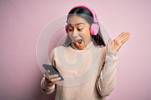 Young beautiful asian woman listening to music using smartphone and headphones very happy and excited, winner expression