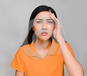 Young beautiful asian woman,long black hair, wore orange t shirt, Showing Headache expression, angry on gray background