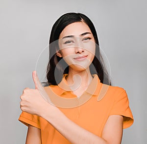 Young beautiful asian woman,long black hair, wore orange t shirt,smile and show Excellent thumbs up on gray background