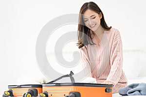 Young beautiful Asian woman packing clothes into suitcase bag on her bed for a vacation. Summer vacation, travel, tourism and