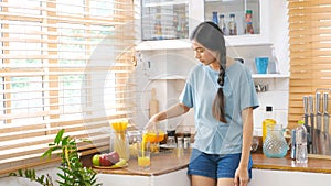 Young beautiful asian woman pouring orange juice on glass while standing in kitchen background, Asian girl drinking orange juice