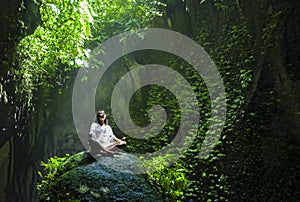 Young beautiful Asian woman practicing Yoga posing sitting in lotus position meditating over a stone in a stunning natural landsca