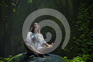 Young beautiful Asian woman practicing Yoga posing sitting in lotus position meditating over a stone in a stunning natural landsca