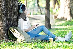 Young beautiful Asian woman relaxing and listening to music using headphones on grass in park. Lifestyle and Relax Concept.