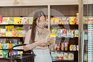 Young beautiful Asian woman shopping and choosing items in supermarket. Female white collar worker picking drink at