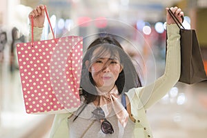 Young beautiful Asian woman shopping at modern mall - happy and attractive Chinese girl holding shopping bags smiling excited