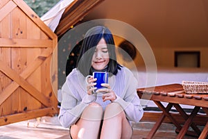 Young beautiful asian woman sitting at tent and drinking coffee in the morning,Enjoys of resting time,Happy and smiling