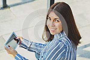 Young beautiful Asian woman smiling at the camera and holding a tablet in her hands