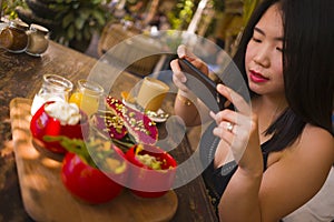 Young beautiful Asian woman takes picture of food  with phone for internet blog. Chinese girl posting online photo for vegetarian