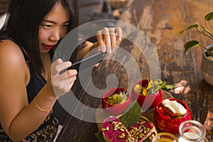 Young beautiful Asian woman takes picture of food  with phone for internet blog. Chinese girl posting online photo for vegetarian