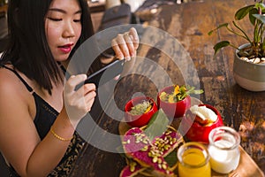 Young beautiful Asian woman takes picture of food with phone for internet blog. Korean girl posting online photo for vegetarian