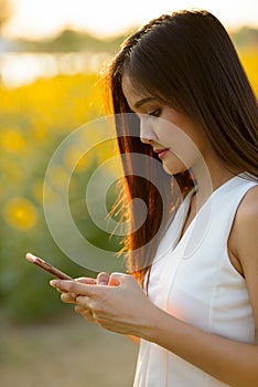 Young beautiful Asian woman using mobile phone against field of