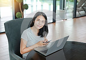 Young beautiful asian woman using mobile phone and laptop computer working online at home and feel relaxing on armchair