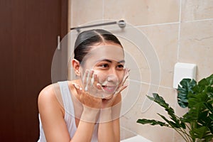 Young beautiful asian woman washing her face with hands by soap