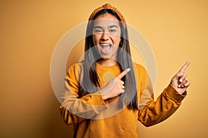 Young beautiful asian woman wearing casual sweater and diadem over yellow background smiling and looking at the camera pointing