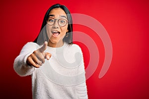 Young beautiful asian woman wearing casual sweater and glasses over red background pointing displeased and frustrated to the