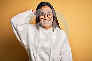 Young beautiful asian woman wearing casual sweater and glasses over yellow background confuse and wonder about question