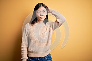 Young beautiful asian woman wearing casual sweater over yellow isolated background confuse and wondering about question