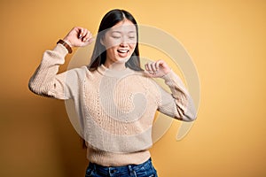 Young beautiful asian woman wearing casual sweater over yellow isolated background Dancing happy and cheerful, smiling moving