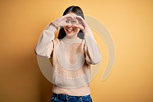 Young beautiful asian woman wearing casual sweater over yellow isolated background Doing heart shape with hand and fingers smiling