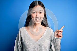 Young beautiful asian woman wearing casual sweater standing over blue isolated background with a big smile on face, pointing with