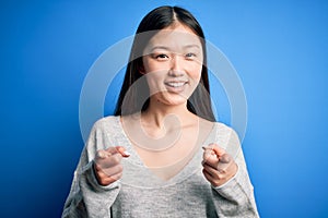 Young beautiful asian woman wearing casual sweater standing over blue isolated background pointing fingers to camera with happy