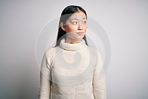 Young beautiful asian woman wearing casual sweater standing over isolated background smiling looking to the side and staring away