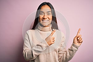 Young beautiful asian woman wearing casual turtleneck sweater over pink background smiling and looking at the camera pointing with