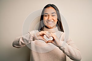 Young beautiful asian woman wearing casual turtleneck sweater over white background smiling in love showing heart symbol and shape