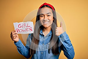 Young beautiful asian woman wearing diadema holding banner with girl power message happy with big smile doing ok sign, thumb up