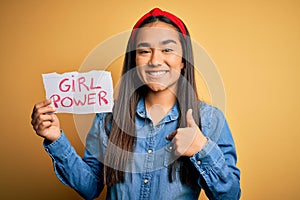 Young beautiful asian woman wearing diadema holding banner with girl power message with surprise face pointing finger to himself