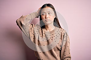 Young beautiful asian woman wearing fashion and elegant sweater over pink solated background confuse and wondering about question