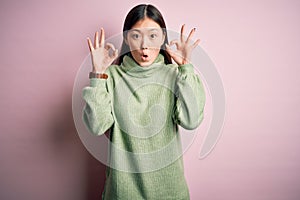Young beautiful asian woman wearing green winter sweater over pink solated background looking surprised and shocked doing ok