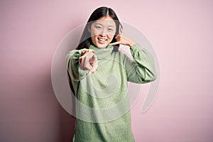 Young beautiful asian woman wearing green winter sweater over pink solated background smiling doing talking on the telephone