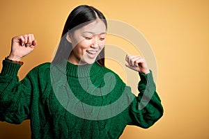 Young beautiful asian woman wearing green winter sweater over yellow isolated background Dancing happy and cheerful, smiling