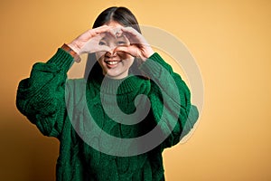 Young beautiful asian woman wearing green winter sweater over yellow isolated background Doing heart shape with hand and fingers