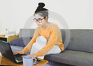 Young beautiful asian woman wore orange knitwear, sitting on gray sofa ,work online lifestyle,relax at home with coffee mug,home