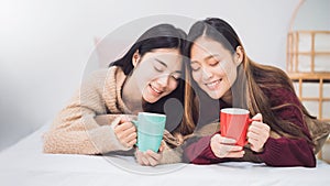 Young beautiful Asian women lesbian couple lover holding coffee cup in bed room at home with smiling face.Concept of LGBT