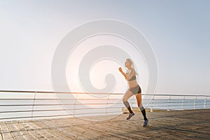 Young beautiful athletic girl with long blond hair in black clothes running at sunrise over the sea