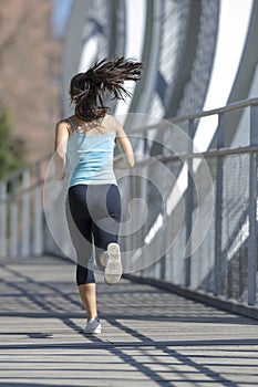 Young beautiful athletic sport woman running and jogging crossing modern metal city bridge