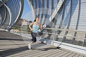 Young beautiful athletic sport woman running and jogging crossing modern metal city bridge