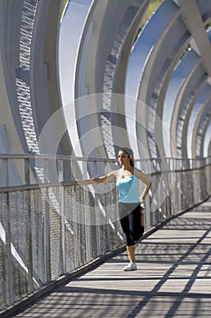 Young beautiful athletic sport woman stretching after running crossing modern metal city bridge