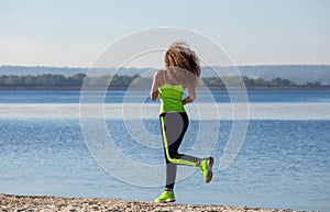 Young, beautiful, athletic woman with long curly hair in the morning runs on the beach, by the lake.