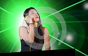 Young beautiful and attractive Asian Korean DJ woman remixing music at night club wearing headphones isolated on flashes and laser