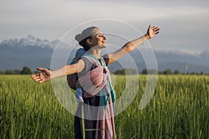 Young beautiful babywearing mother carry her newborn baby in a ring sling in rural field scene