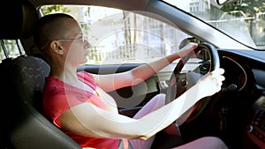 Young beautiful bald woman in sunglasses sitting at the wheel of a car on a summer day. Car trip