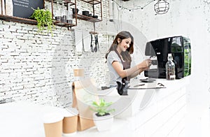 Young beautiful barista female in an apron preparing cup of coffee for customer in coffee shop. Woman startup business owner and