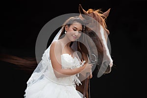 Young beautiful beauty bride in fashion white wedding costume stand with handsome horse on black background