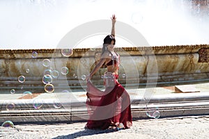 A young and beautiful belly dancer dancing in a square. She is dressed in light blue with a white veil in her hands. World